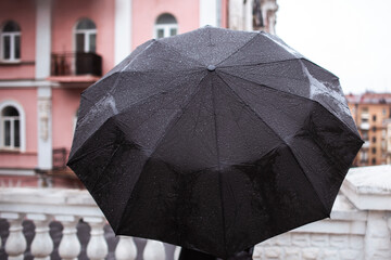 unknown person standing from behind with black big umbrella on old style buildings