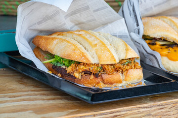 The perfect sandwich with cheese, bacon, pickles, tomatoes, onions and turnips for sale at the counter of a van at a food truck