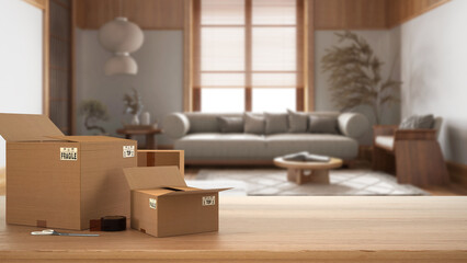 Wooden table, desk or shelf with stack of cardboard boxes over blurred view of japandi living room in minimal style, interior design, moving house concept with copy space