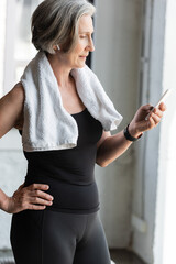 Fototapeta na wymiar fit senior woman with towel on shoulders using smartphone while listening music in wireless earphone.