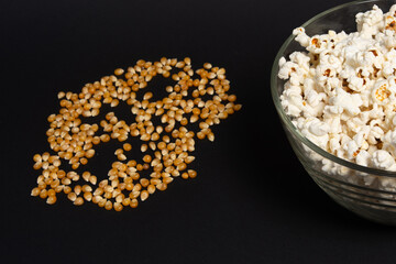 Obraz na płótnie Canvas A bowl of fried popcorn and corn kernels on a black background