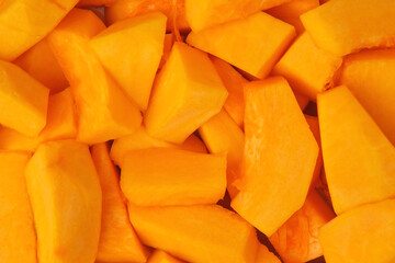 Slices of fresh pumpkin chunks background. Yellow Juicy pieces of pumpkin. Texture close up. Full frame with copy space for text, label. Food backdrop. Bright orange sliced pumpkin