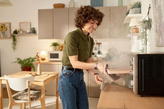 Young housewife taking burnt food out of the oven during cooking in the kitchen at home