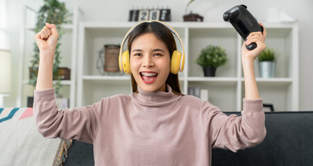 Excited Young Asian woman holding joysticks with playing online game with fists clenched...
