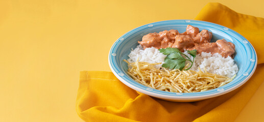 Chicken strogonoff with rice and potato straw on yellow background with copy space
