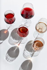 Top view of glasses filled with delicious red, rose and white wine standing against white background with reflection. Concept of taste, alcohol, wine degustation, variety, winemaking. Flat lay
