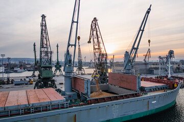 Fototapeta na wymiar Black Sea Grain Initiative 2023 grain Deal. Silhouettes of port cranes during the loading of grain on a bulk carrier at sunset during the golden hour. Panoramic flight from a drone