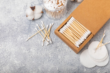 Fototapeta na wymiar Cotton swabs in craft packaging and holder on a gray cement background. Bamboo cotton buds. Means for hygiene of ears. Eco-friendly materials.Hygienic cotton ear buds.