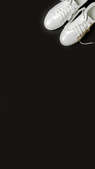 White leather shoes on a black background. White sneakers with white laces. New shoes. Vertical image.