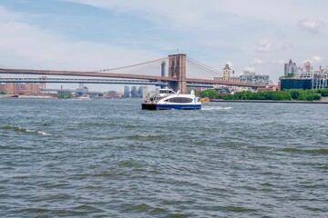 Daytime view of tour boat riding on East River with Brooklyn bridge in background