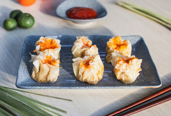 Steamed chicken dimsum served on plate with chili, tomato and sauce as background on wooden table