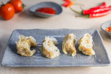 Steamed dimsum served on plate with chili, tomato and sauce as background on wooden table