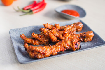 Spicy chicken feet or ceker ayam pedas with chili, tomato and sauce served with a plate on wooden white table