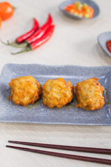 Fried prawn dimsum (udang rambutan) served on plate with chili, tomato and sauce as background on wooden table