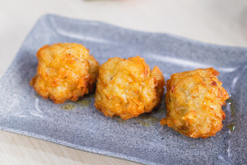 Fried prawn dimsum (udang rambutan) served on plate with chili, tomato and sauce as background on wooden table