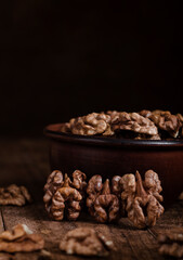 Organic dried walnut kernels next to the ceramic bowl on a dark wooden table. Walnut kernels close up. Brain food