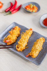 Fried prawn dimsum (udang rambutan) served on plate with chili, tomato and sauce as background on wooden table