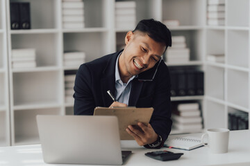 Fototapeta premium Happy working asian businessman talking on the phone with accounting documents at desk in happy working office
