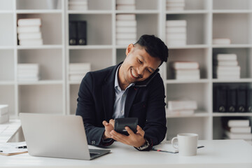 Naklejka premium Happy working asian businessman talking on the phone with accounting documents at desk in happy working office