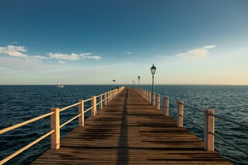 Long wooden pier surrounded by the clam waters of the blue ocean with the horizon in the background