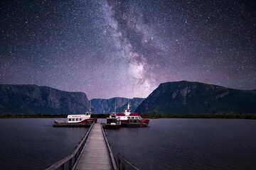 Scenic view of a ferry moored at a pier on a lake on a background of mountains and starry night sky