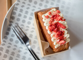 Close-up top view of red iced strawberries and soft cream on brown cake or croissant bread, sweet dessert with a fork on wood table background in cafe.