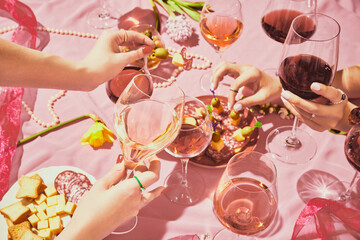 Holidays meeting. Female hands with glassed with red and rose wine on pink textured background,...
