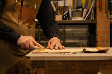 senior leather craftsman while crushing the seams of a leather back of a chair made by him in his workshop on an old workbench
