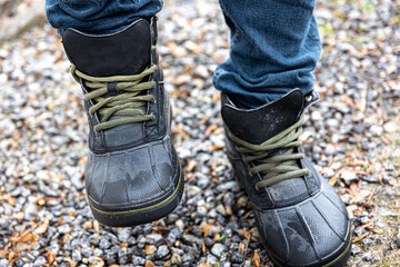 A man in boots stands on gravel, close up.