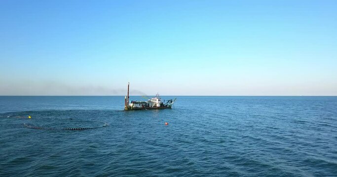 Ship on the sea is grating the sand with the pipes under water