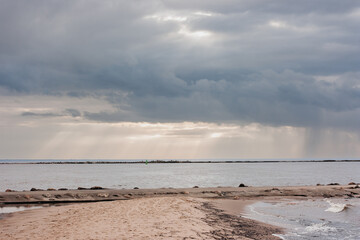 seashore with a sand embankment leading to the jetty. dramatic sky with clouds through which the rays of the sun shine.