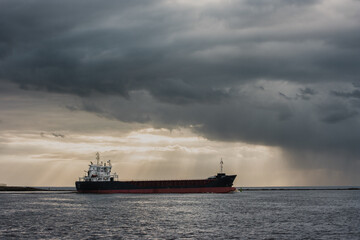 view of a tanker sailing across the sea under a dramatic dark sky with golden sunlight shining through the clouds.