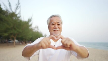 Portrait of Happy Asian senior man showing hands heart shape during walking at tropical beach at summer sunset. Retired elderly people enjoy outdoor lifestyle travel nature ocean on holiday vacation. - Powered by Adobe