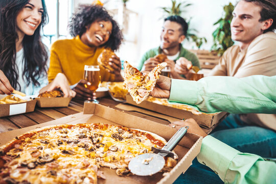 Multiracial happy friends eating pizza together at home - Young people having dinner party in house balcony - Delivery food concept with guys and girls dining in apartment