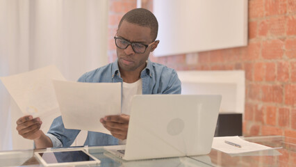 Reading Document by African Man and Working on Laptop
