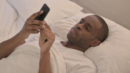 African Man using Smartphone while Lying in Bed