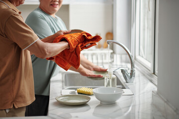 Senior woman washing dished and husband wiping with sof towel