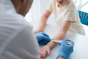A male doctor makes an important Mantoux test on a child. The doctor measures the Mantoux test with a ruler for a little boy