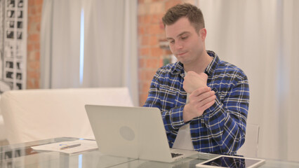 Young Casual Man with Wrist Pain Working on Laptop 