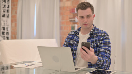 Young Casual Man Working on Laptop and Using Smartphone