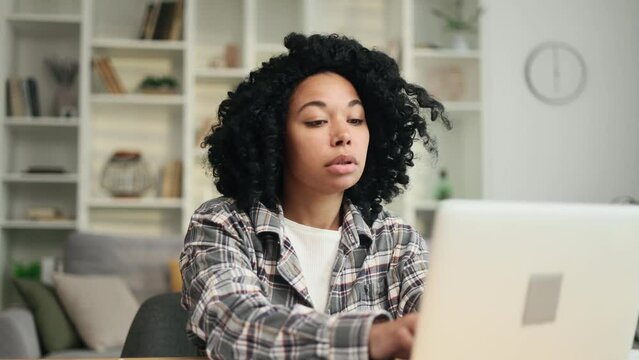 Sad african american woman student or freelancer with lack of new ideas or creative block typing deleting text on laptop computer and looking at camera with worried face at home