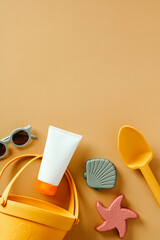 Kids sunscreen cream tube, sand molds, sunglasses on sand color background