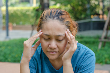 Asian women sitting at park touch their temples, feel a headache or dizzy, feeling tired. need...