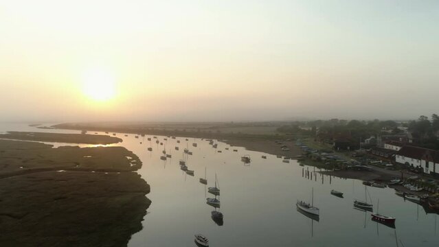 Establishing Aerial Drone Shot Flying Over Burnham Overy Staithe Coastal Village Creek with Boats at Stunning Foggy Sunrise into the Sun North Norfolk UK East Coast