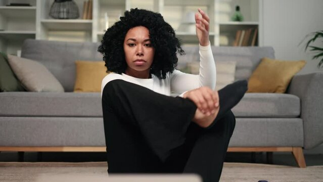Funny african american young woman with puzzled face looks at hard fitness sport workout of online trainer unsuccessfully tries to repeat and looking at camera shrugs at home alone Beginner concept 