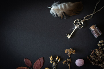 Magic tools on black background, silver key, bottle, feather, dried herbs and rose quartz, copy space.