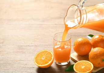 Pouring orange juice into the glass on wooden table.