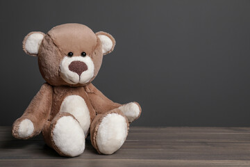 Cute teddy bear on wooden table near black wall, space for text