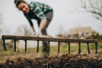 Young woman farmer works with a rake in a field in spring. Preparing the soil before planting....