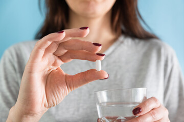 Woman taking white pill of statin medicine to treat high cholesterol or painkiller with glass of water on blue background